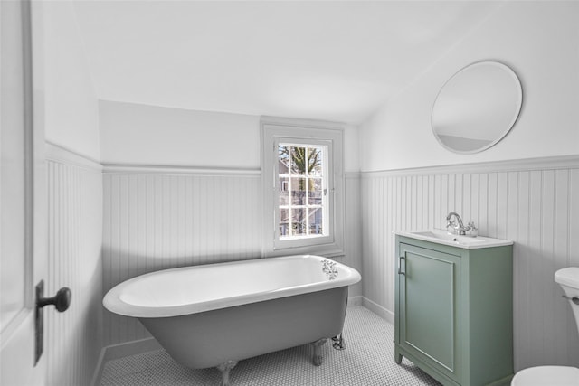 full bath with a wainscoted wall, vanity, toilet, and a soaking tub