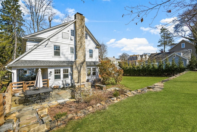 rear view of property with a patio area, a lawn, a chimney, and a shingled roof