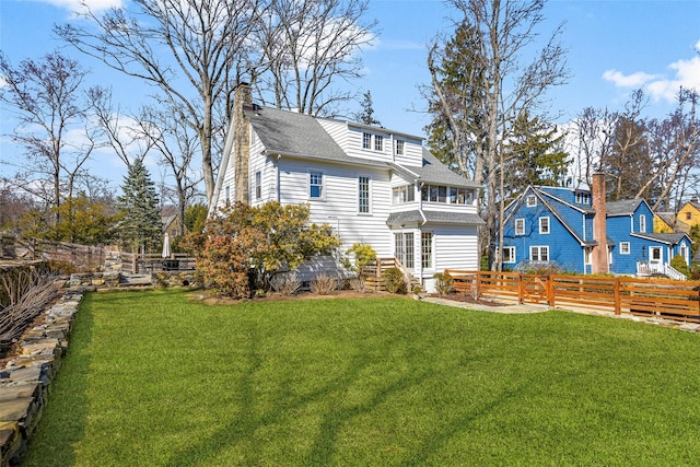 rear view of house featuring a lawn, a chimney, and fence