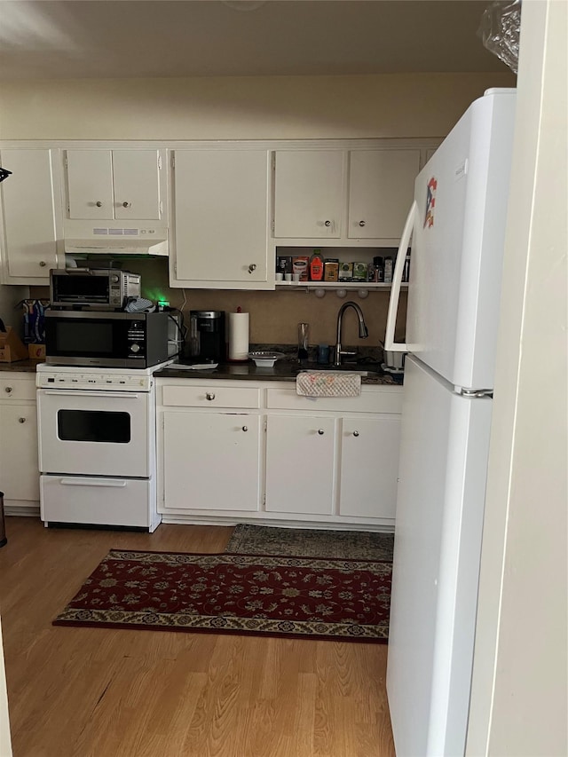 kitchen featuring dark countertops, white appliances, a sink, and wood finished floors