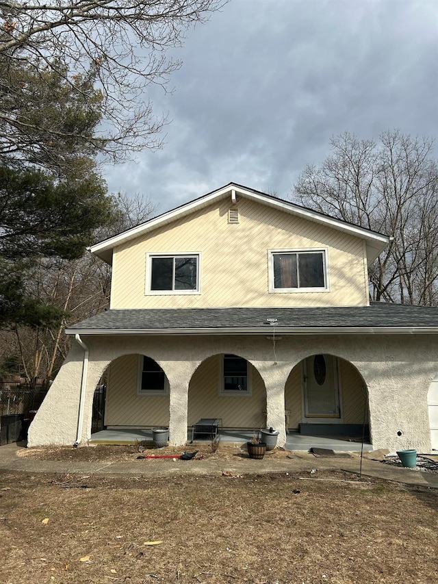 rear view of property with covered porch and roof with shingles