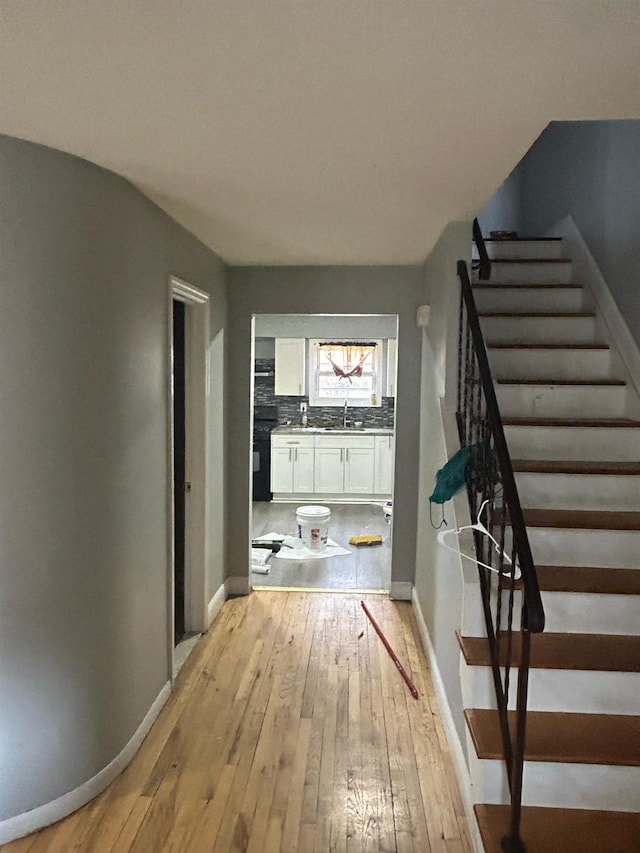 corridor with light wood finished floors, stairway, a sink, and baseboards