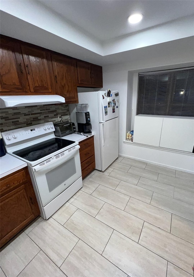 kitchen with backsplash, under cabinet range hood, light countertops, recessed lighting, and white appliances