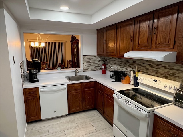 kitchen with under cabinet range hood, light countertops, decorative backsplash, white appliances, and a sink