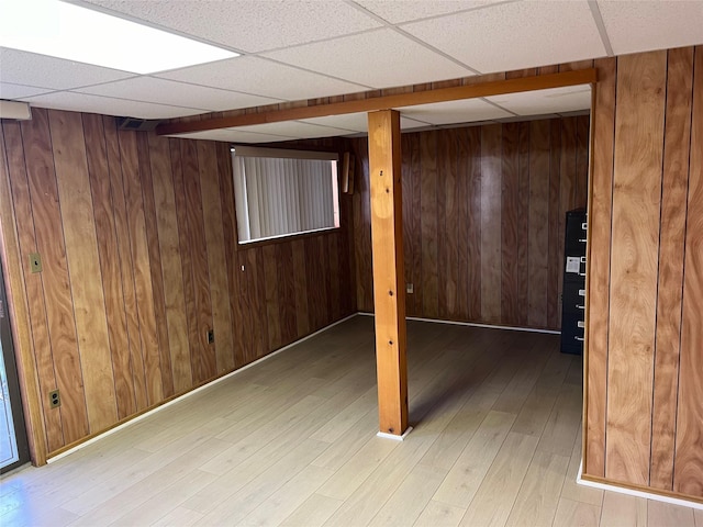 finished below grade area with a drop ceiling, light wood-style flooring, and wood walls