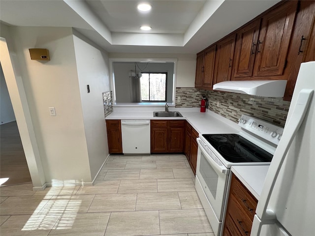 kitchen with under cabinet range hood, light countertops, decorative backsplash, white appliances, and a sink