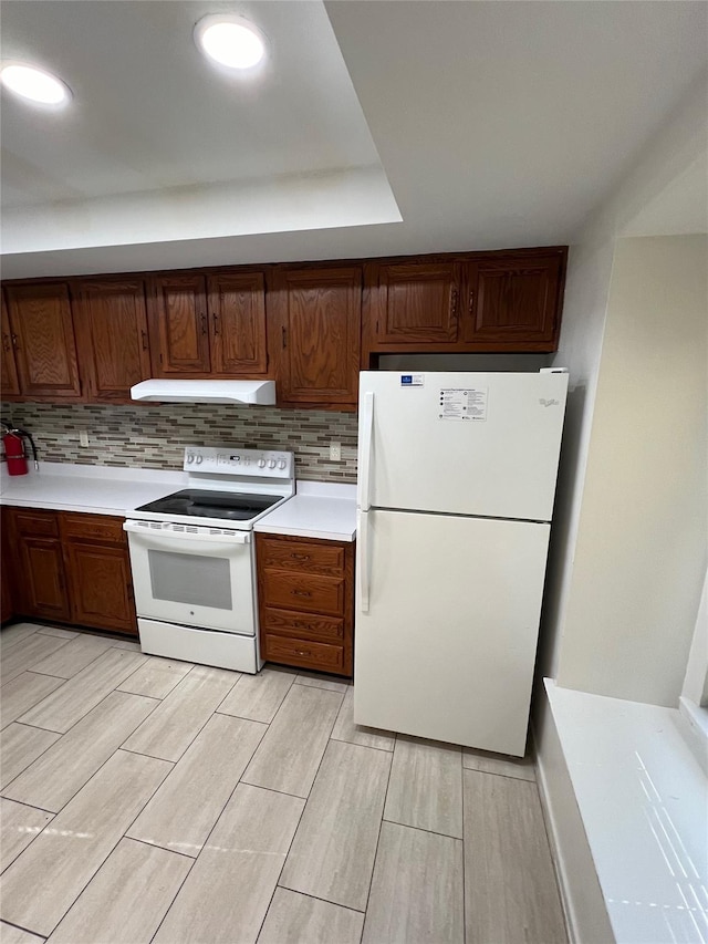 kitchen featuring under cabinet range hood, white appliances, backsplash, and light countertops