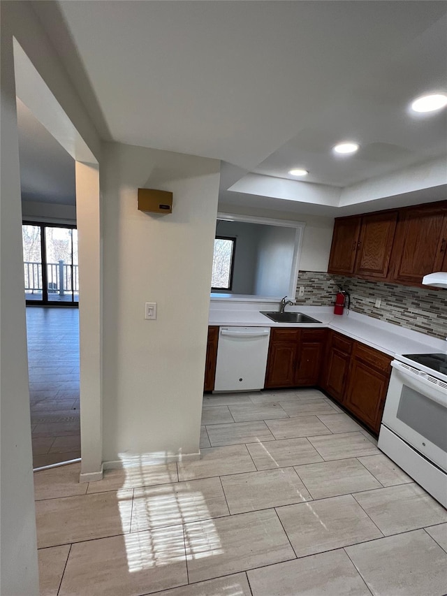 kitchen featuring a sink, decorative backsplash, white appliances, and light countertops