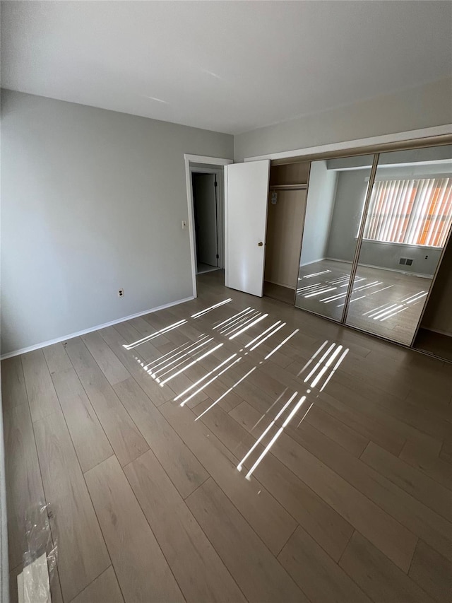 unfurnished bedroom featuring a closet, visible vents, baseboards, and wood finished floors