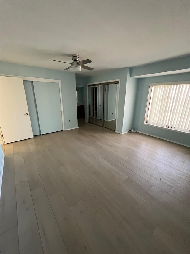 unfurnished bedroom with a ceiling fan, wood finished floors, multiple closets, and baseboards