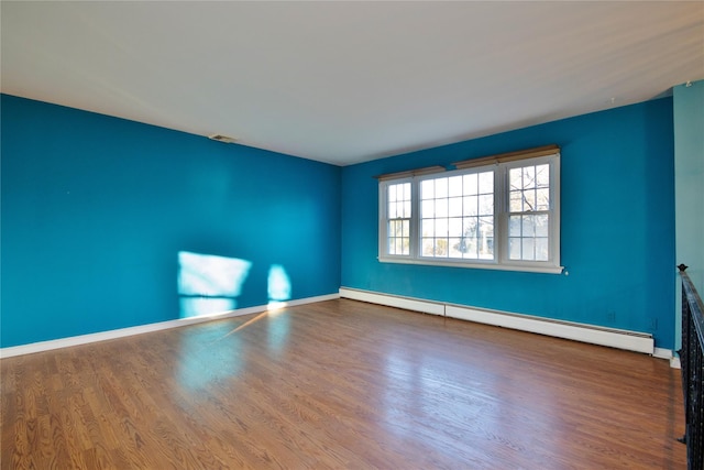 spare room featuring a baseboard radiator, baseboards, visible vents, and wood finished floors