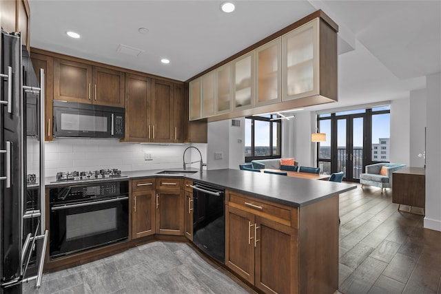 kitchen featuring dark countertops, backsplash, a peninsula, black appliances, and a sink