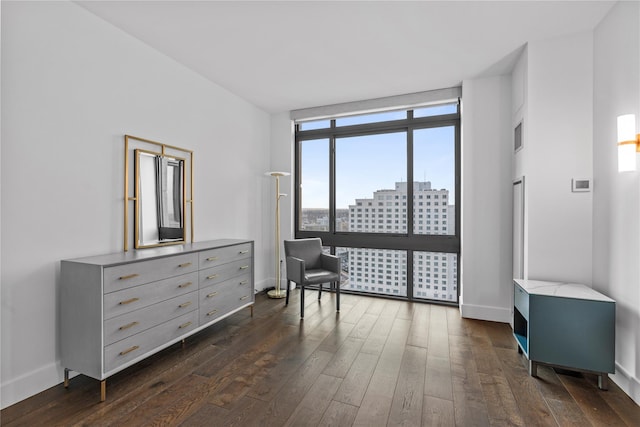 sitting room featuring a view of city, a wall of windows, dark wood finished floors, and baseboards