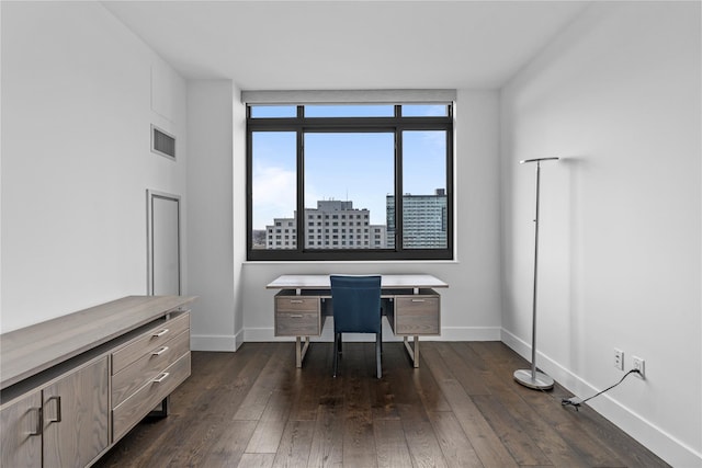 unfurnished office with dark wood-style floors, baseboards, visible vents, and a city view