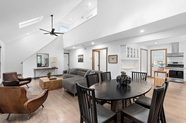 dining space with ceiling fan, high vaulted ceiling, recessed lighting, a skylight, and light wood-style floors