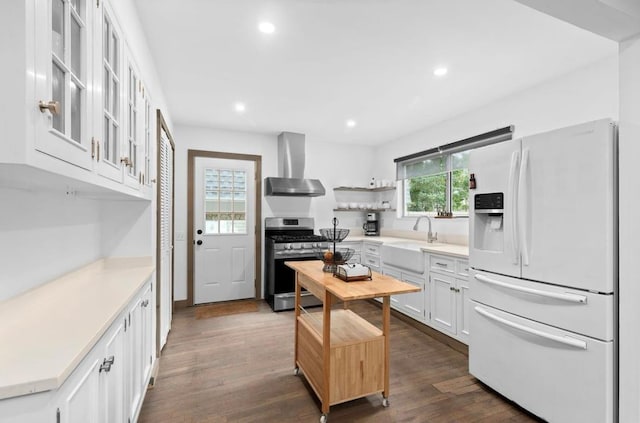 kitchen featuring white refrigerator with ice dispenser, dark wood finished floors, wall chimney exhaust hood, a sink, and gas stove