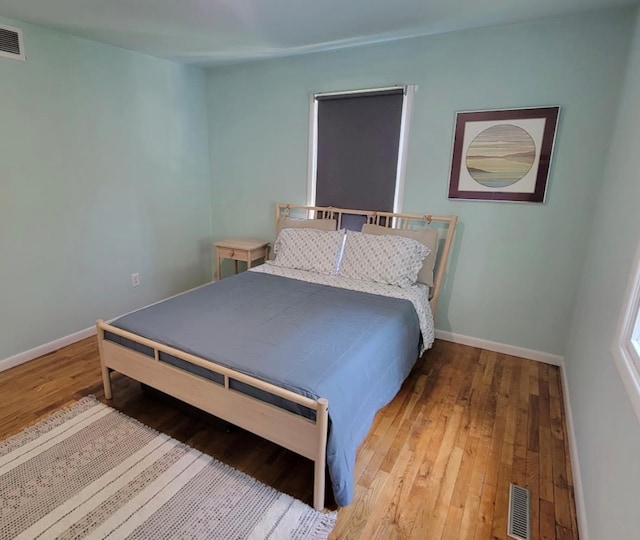 bedroom with hardwood / wood-style floors, visible vents, and baseboards