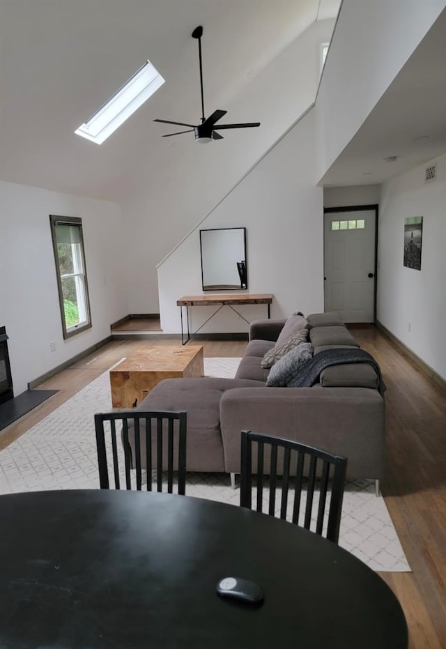 dining space featuring a skylight, baseboards, ceiling fan, wood finished floors, and high vaulted ceiling