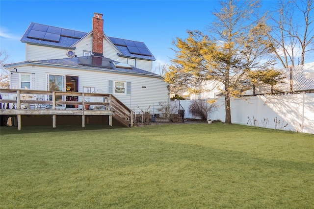 rear view of house with a yard, a chimney, solar panels, a fenced backyard, and a wooden deck