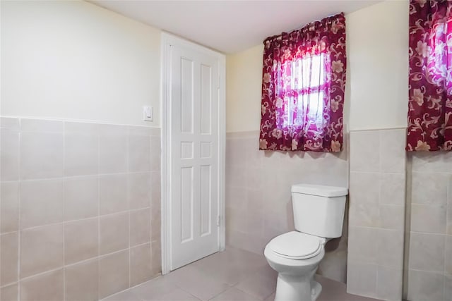 bathroom featuring toilet, a wainscoted wall, tile walls, and tile patterned floors