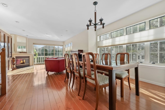 dining space with wood-type flooring, a glass covered fireplace, and an inviting chandelier