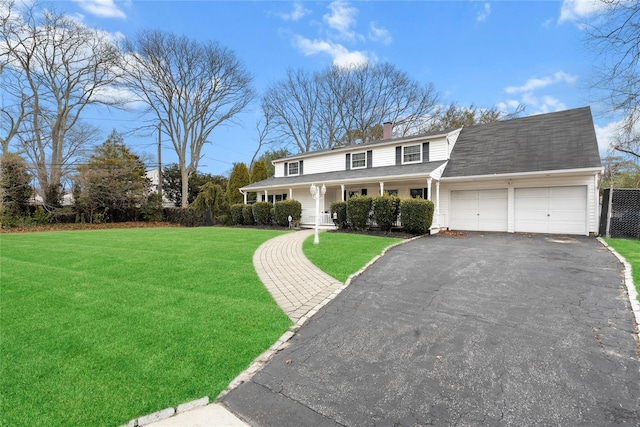 view of front of property with an attached garage, a front yard, covered porch, a chimney, and driveway