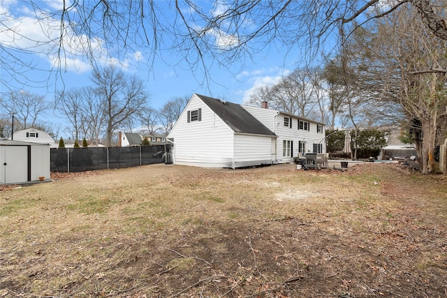 back of property with a storage unit, a lawn, fence, an outdoor structure, and a chimney