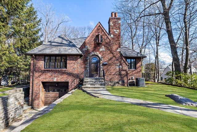 english style home featuring brick siding, an attached garage, a chimney, and a front lawn