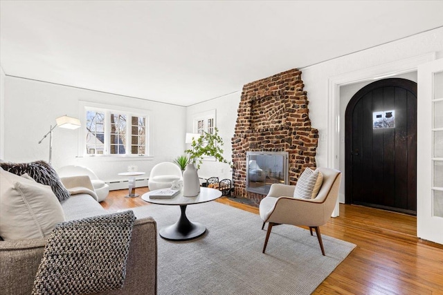 living area with baseboard heating, wood finished floors, and a fireplace