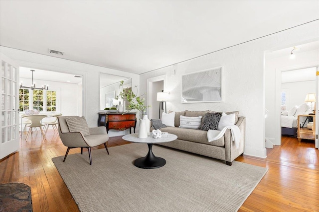 living area with light wood-type flooring, visible vents, and a chandelier