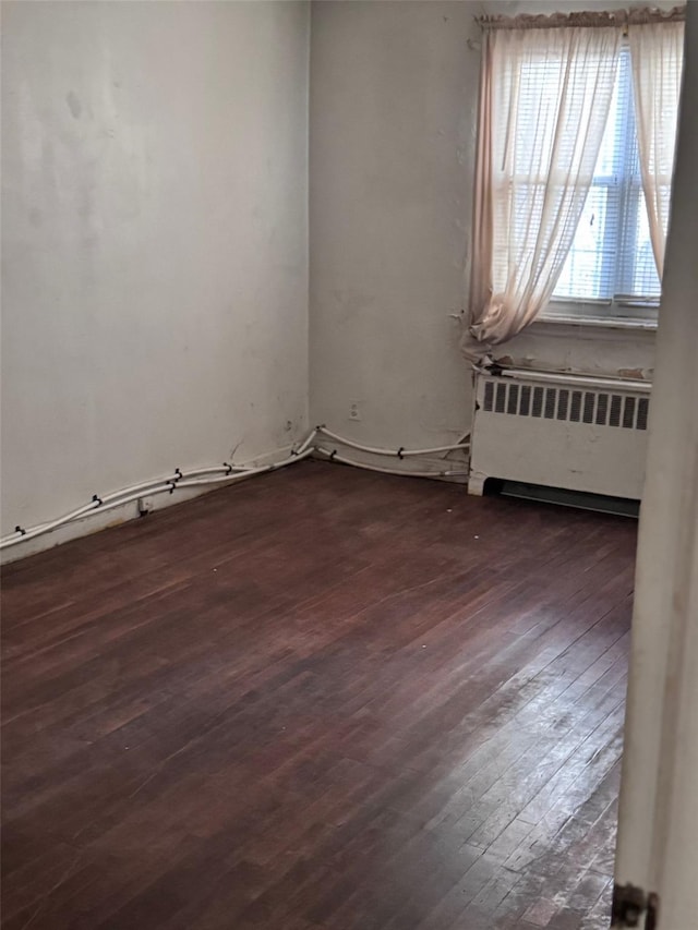 unfurnished room with dark wood-style floors and radiator heating unit