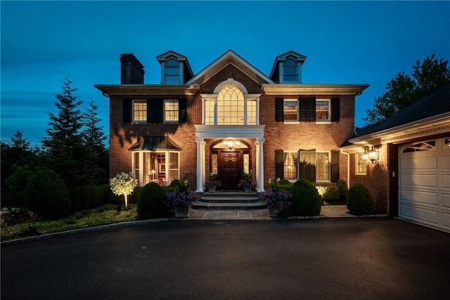 colonial home featuring a garage, driveway, brick siding, and a chimney