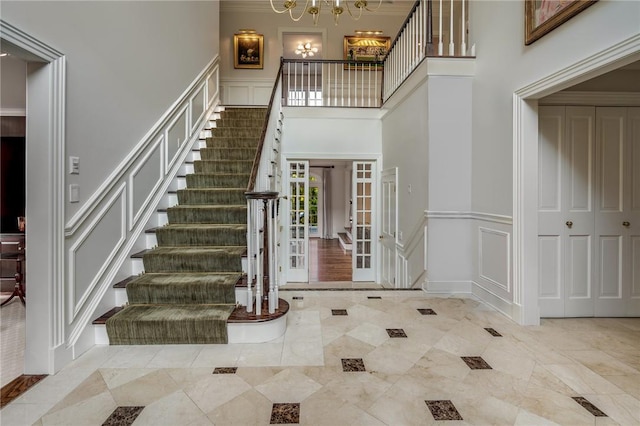 foyer with a chandelier, a decorative wall, a wainscoted wall, a towering ceiling, and stairs