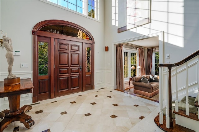 foyer with light tile patterned floors, wainscoting, a towering ceiling, stairway, and a decorative wall