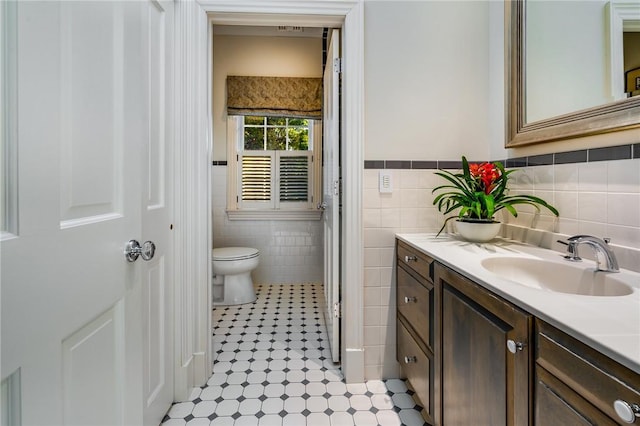 bathroom with a wainscoted wall, vanity, toilet, and tile walls