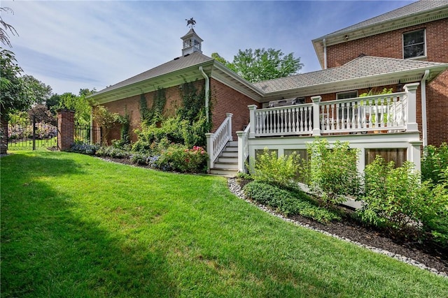 rear view of property with a deck, brick siding, a lawn, and stairway