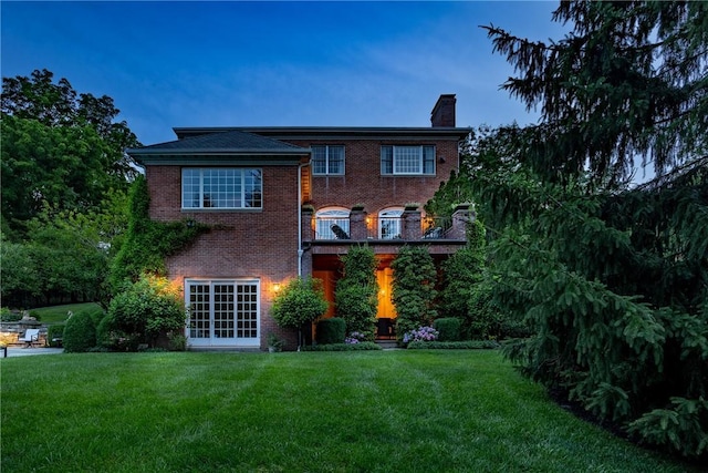 rear view of property with a yard, brick siding, and a chimney