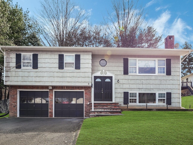 bi-level home featuring a front lawn, an attached garage, a chimney, and aphalt driveway