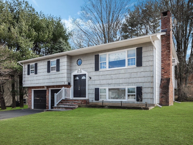 bi-level home with aphalt driveway, an attached garage, a chimney, and a front yard