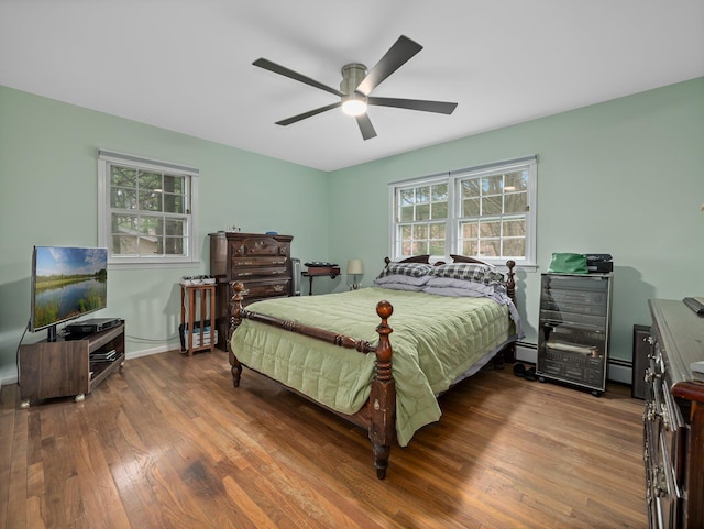 bedroom with baseboard heating, a baseboard heating unit, ceiling fan, and wood finished floors