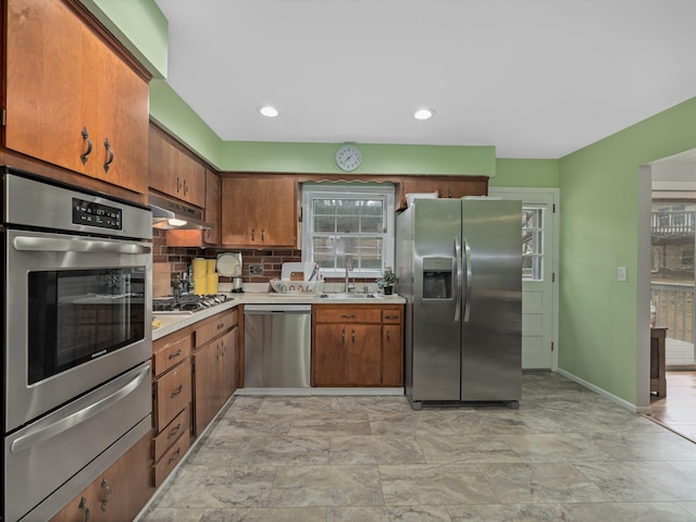 kitchen with under cabinet range hood, light countertops, stainless steel appliances, a warming drawer, and a sink