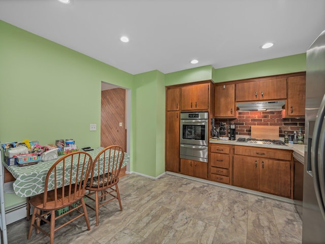 kitchen with backsplash, under cabinet range hood, light countertops, appliances with stainless steel finishes, and a warming drawer