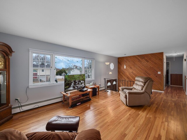 living area with an accent wall, wooden walls, light wood finished floors, and baseboard heating