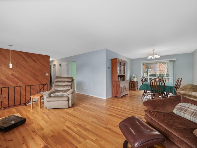 living room featuring light wood-style flooring, wood walls, baseboards, a chandelier, and an accent wall