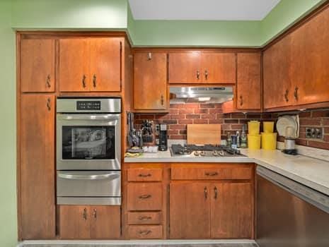 kitchen featuring under cabinet range hood, appliances with stainless steel finishes, a warming drawer, brown cabinets, and backsplash