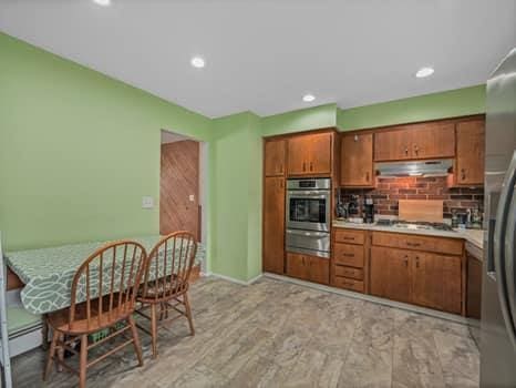 kitchen featuring under cabinet range hood, stainless steel appliances, a warming drawer, and brown cabinetry