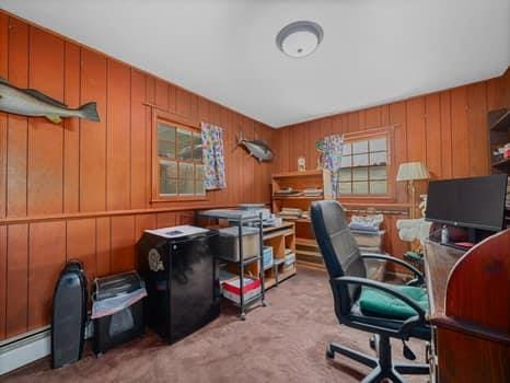 carpeted office space featuring a baseboard heating unit and wooden walls