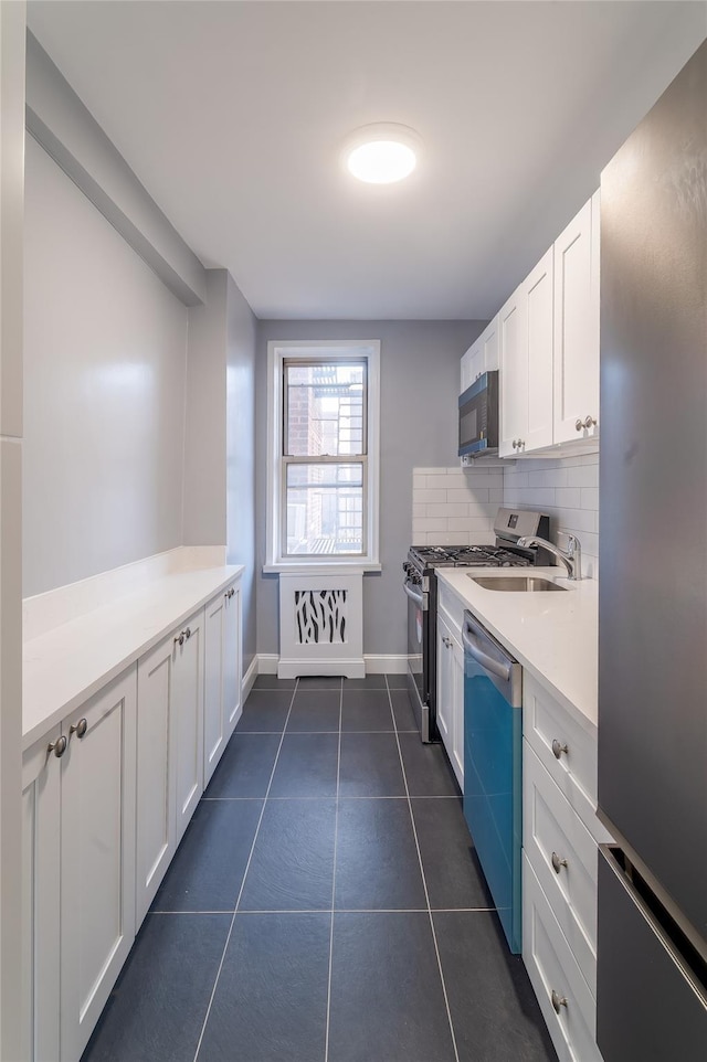 kitchen with tasteful backsplash, light countertops, appliances with stainless steel finishes, white cabinetry, and dark tile patterned floors