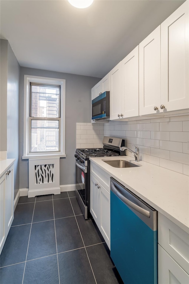 kitchen with dishwasher, dark tile patterned flooring, backsplash, stainless steel range with gas cooktop, and a sink