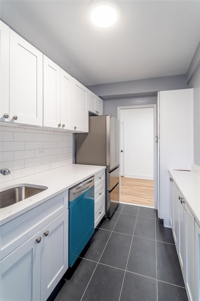 kitchen with white cabinets, dark tile patterned flooring, dishwashing machine, light countertops, and a sink